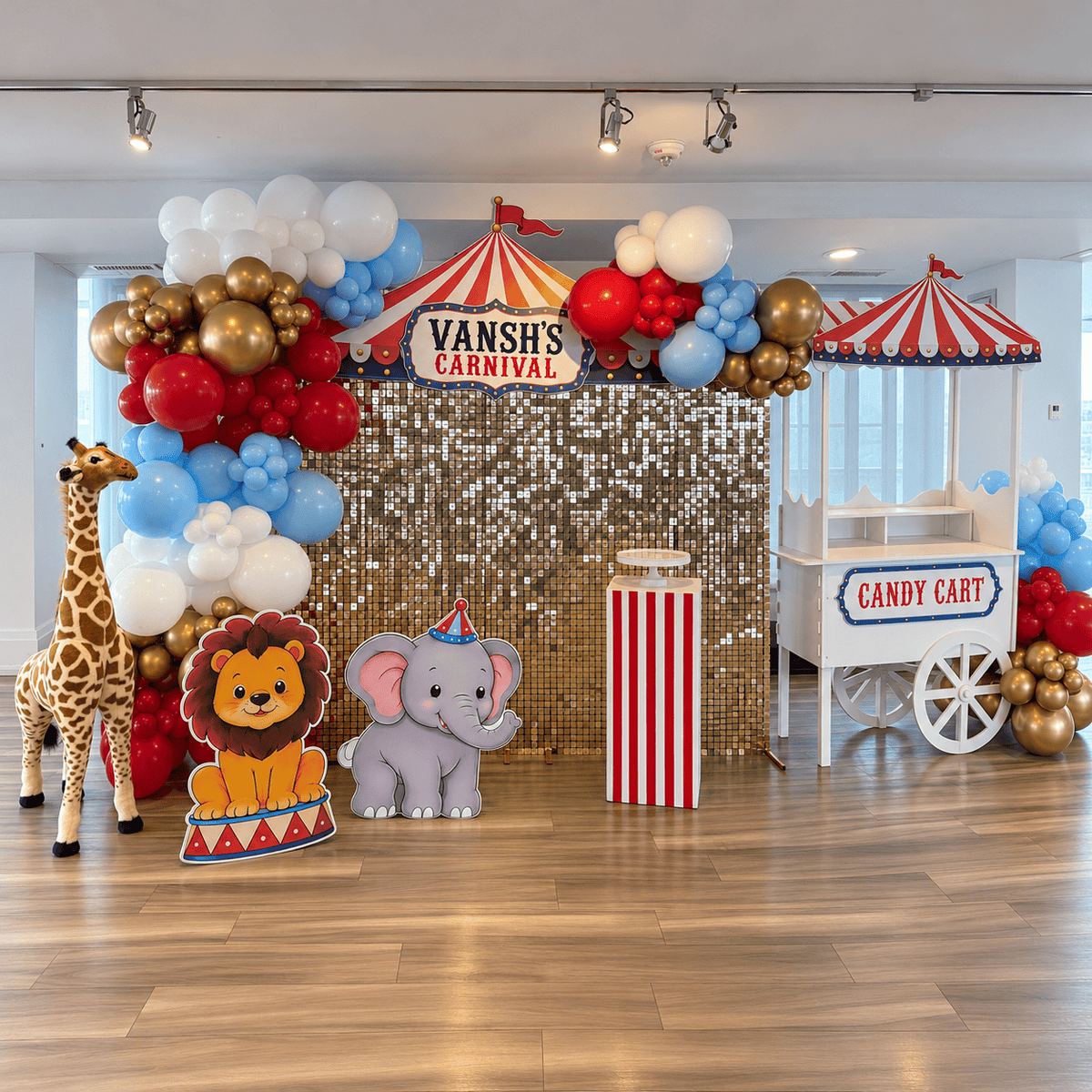 Carnival birthday setup with a gold shimmer wall, colourful balloons, circus tent topper, animal props, striped pedestal, and candy cart.