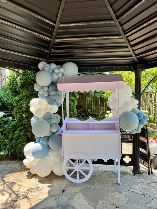 White candy cart with blue and white balloon garland, styled for baby shower or birthday dessert display