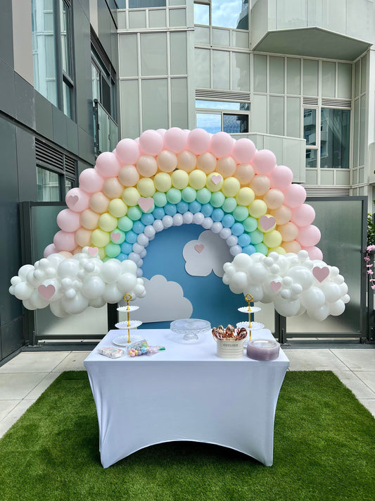 Decorative balloon arch with rainbow and clouds at an outdoor event.