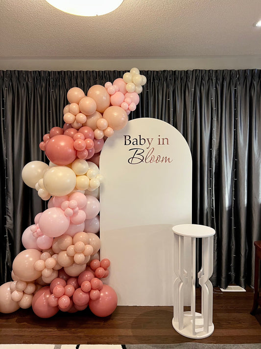 Blush Baby in Bloom backdrop with white oval wall, pink beige and white balloon garland, and matching cake table