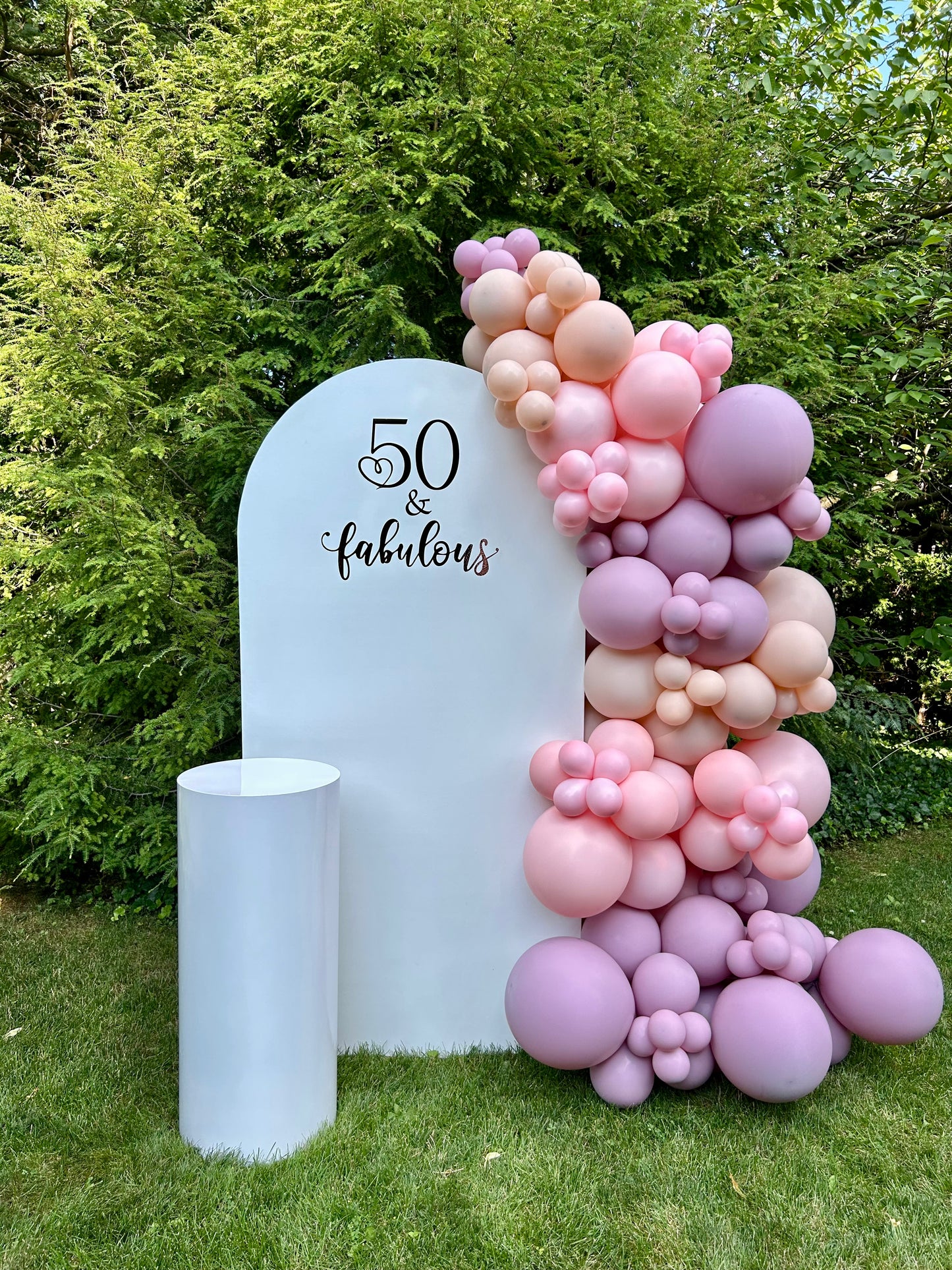 Balloon arch with '50 & fabulous' text against a white backdrop outdoors.