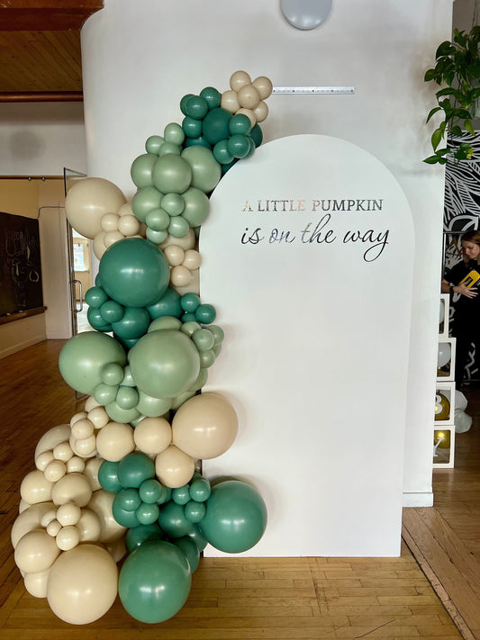 Little Pumpkin on the Way baby shower setup with white oval backdrop, green beige and sage balloon garland