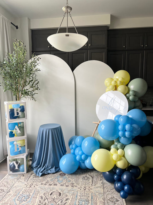First birthday backdrop with two white backdrops, Baby Blocks, cake table and custom balloon sign in blue with yellow, green and navy accents