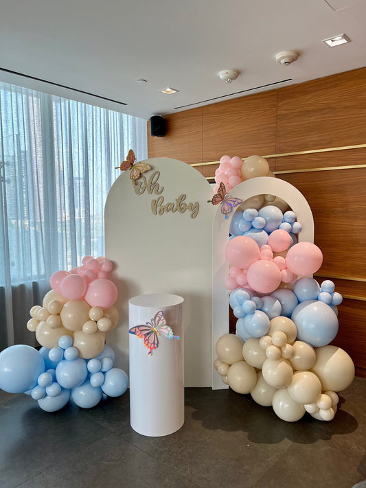 Neutral pastel baby shower backdrop with oval and hollow arch, beige pink & blue balloons, Oh Baby sign, butterflies & cake table