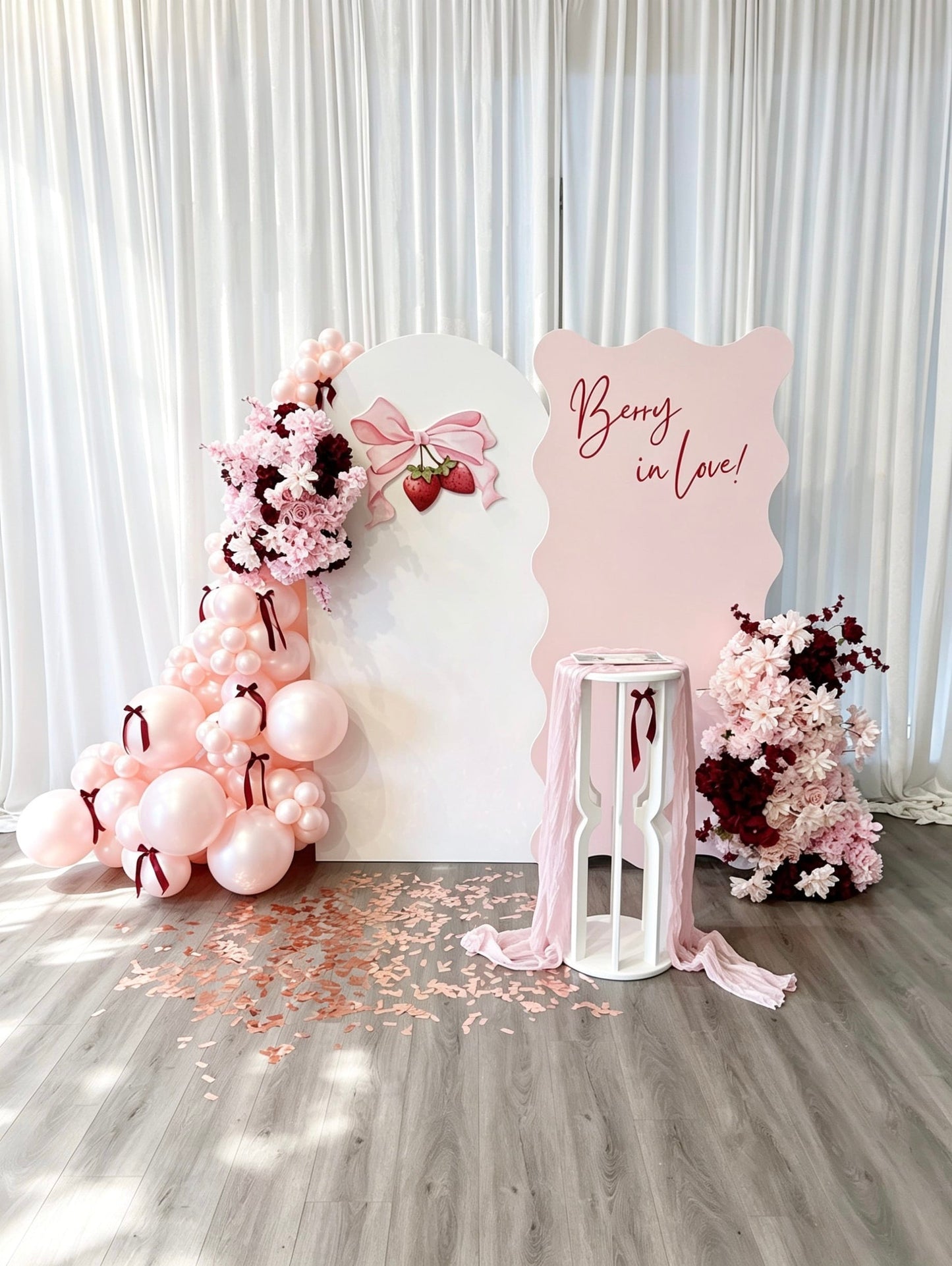Decorative setup with balloons, flowers, and a sign on a wooden floor.