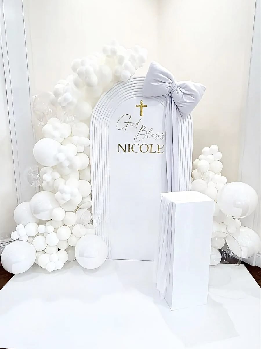 White Communion balloon backdrop with ripple arch panel, oversized bow and organic balloon garlands