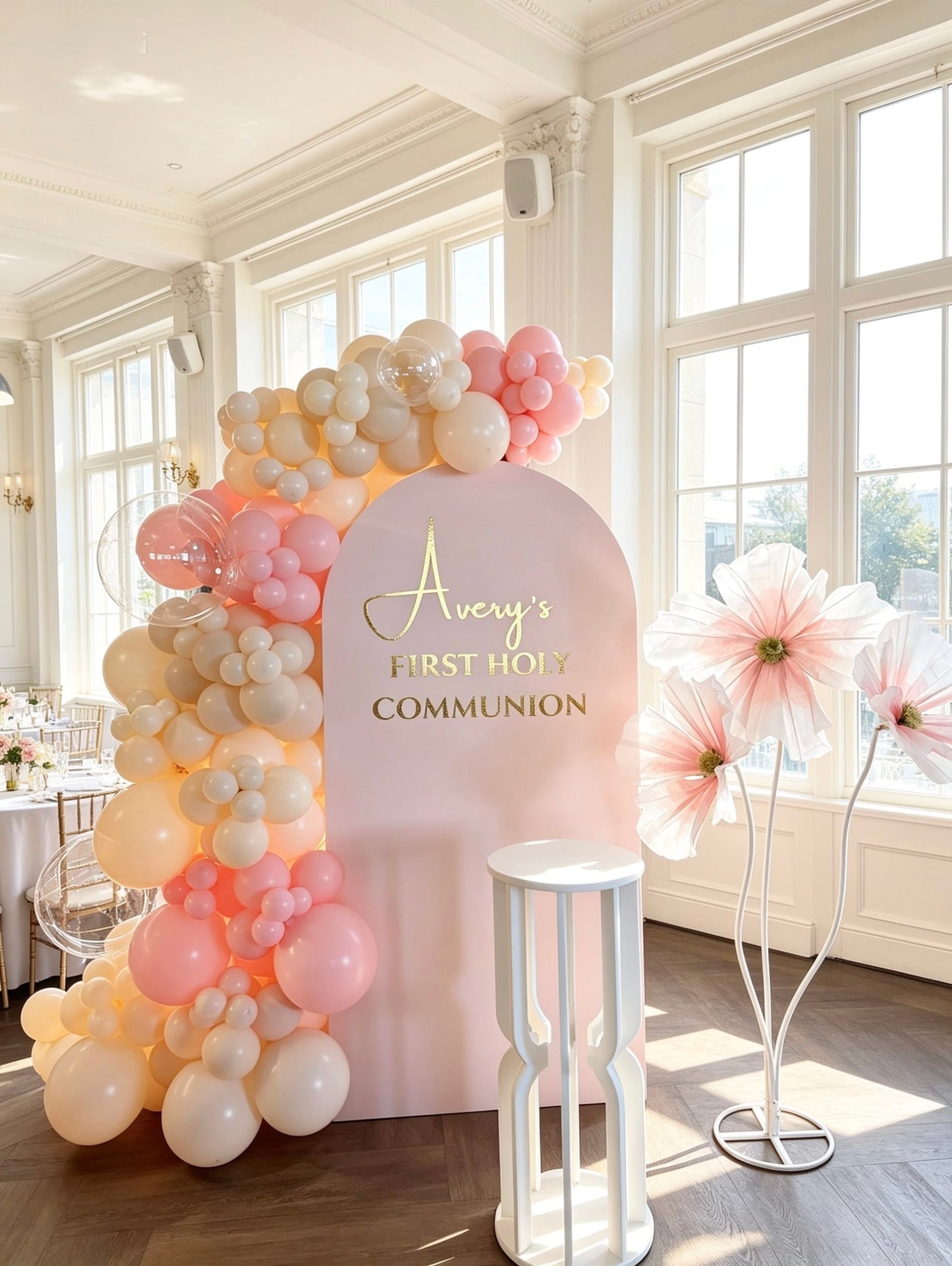 Blush pink First Holy Communion backdrop with organic balloon garland, clear bubble balloons, oversized floral props and custom gold lettering.