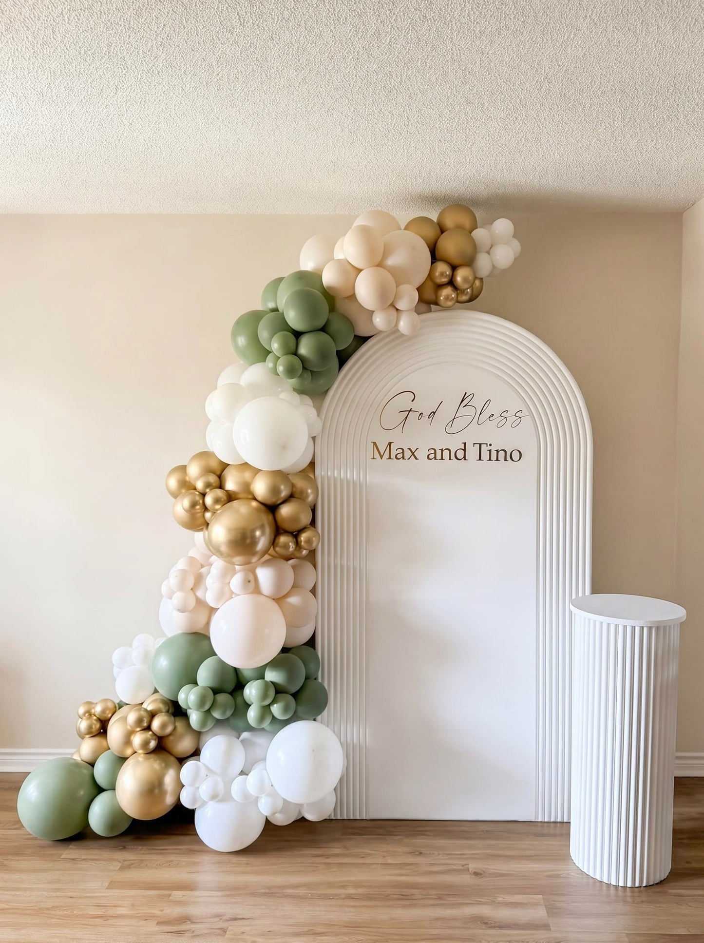 White ripple arch backdrop with sage green, white and gold balloon garland, custom gold lettering and matching pedestal stand.