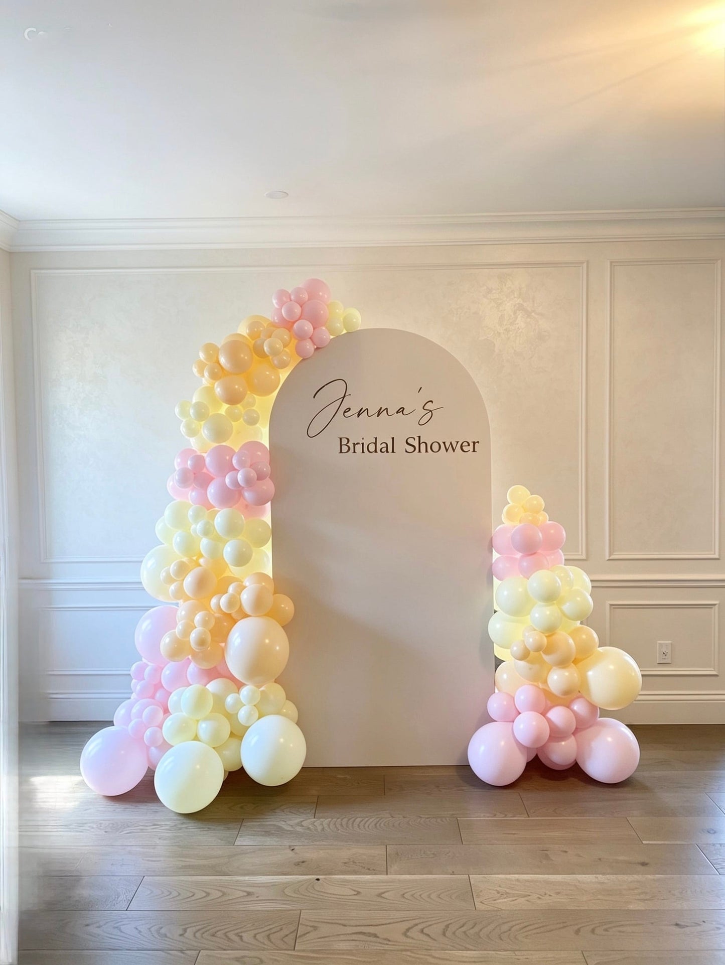 Bridal shower backdrop with pastel yellow and pink balloon garlands around neutral arch panel