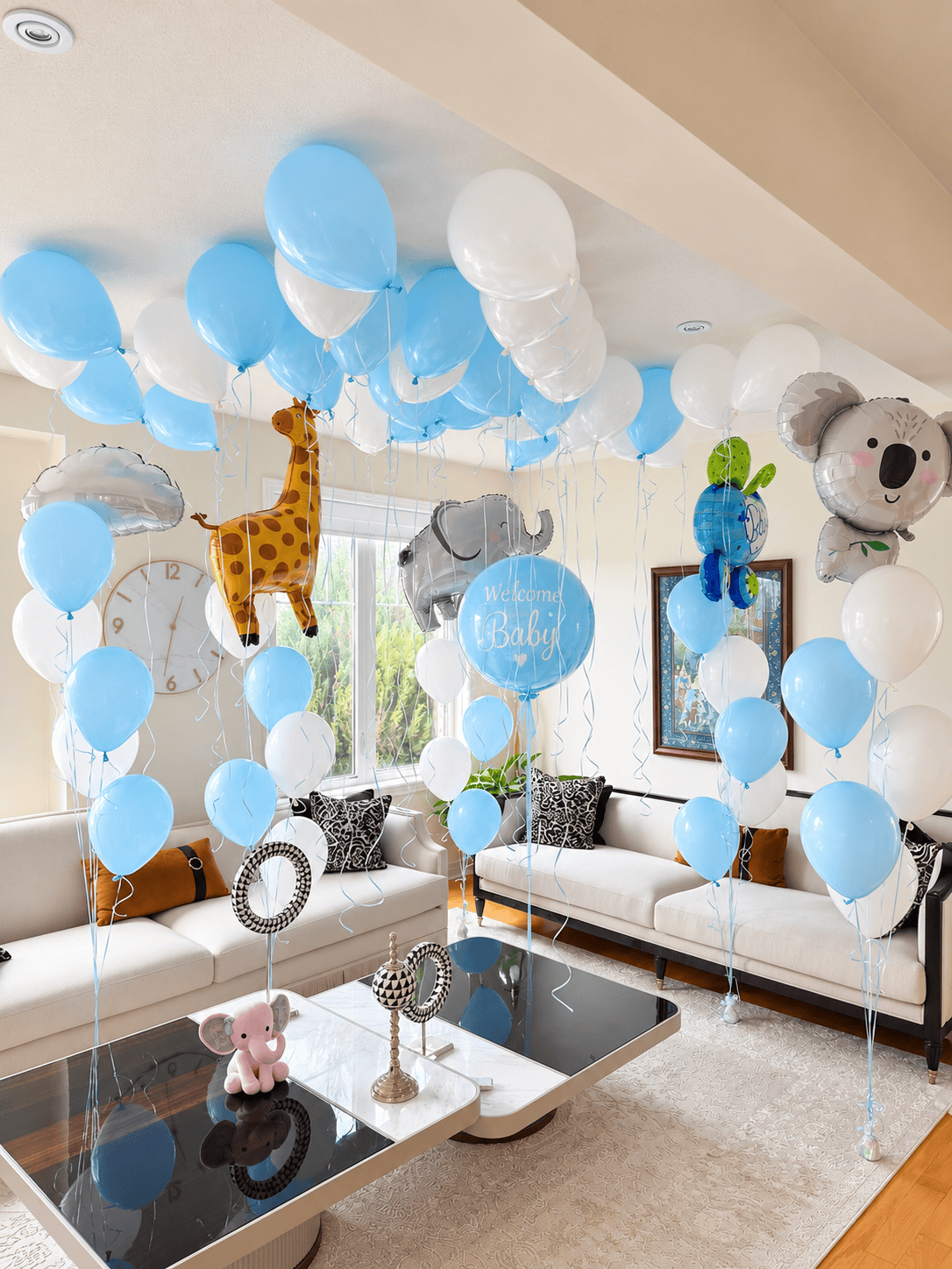 Blue and white welcome-home baby balloon setup with animal foil bouquets, ceiling balloons, and a large “Welcome Baby” balloon.