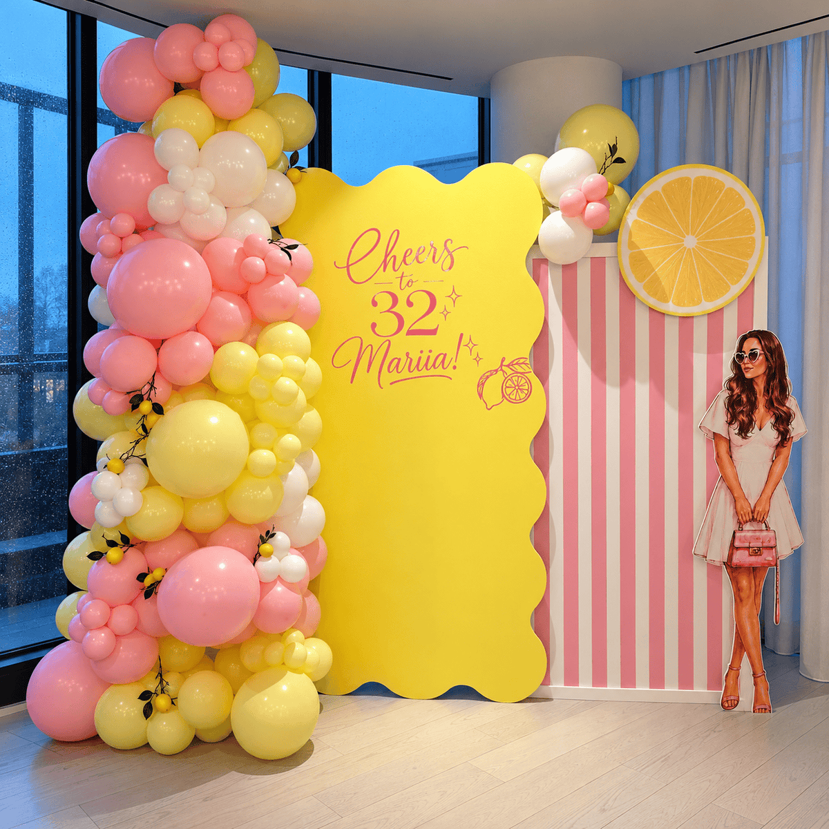 Yellow wavy birthday backdrop with custom lettering, a pink striped panel, pastel balloons, lemon decorations, and a portrait cutout.