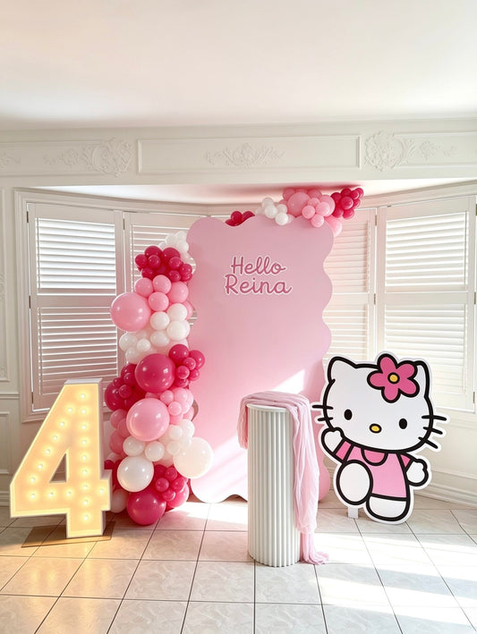 Pink Hello Kitty 4th birthday setup with custom wavy backdrop, pink balloon garland, marquee number 4, white ripple cake table, and Hello Kitty cutout.
