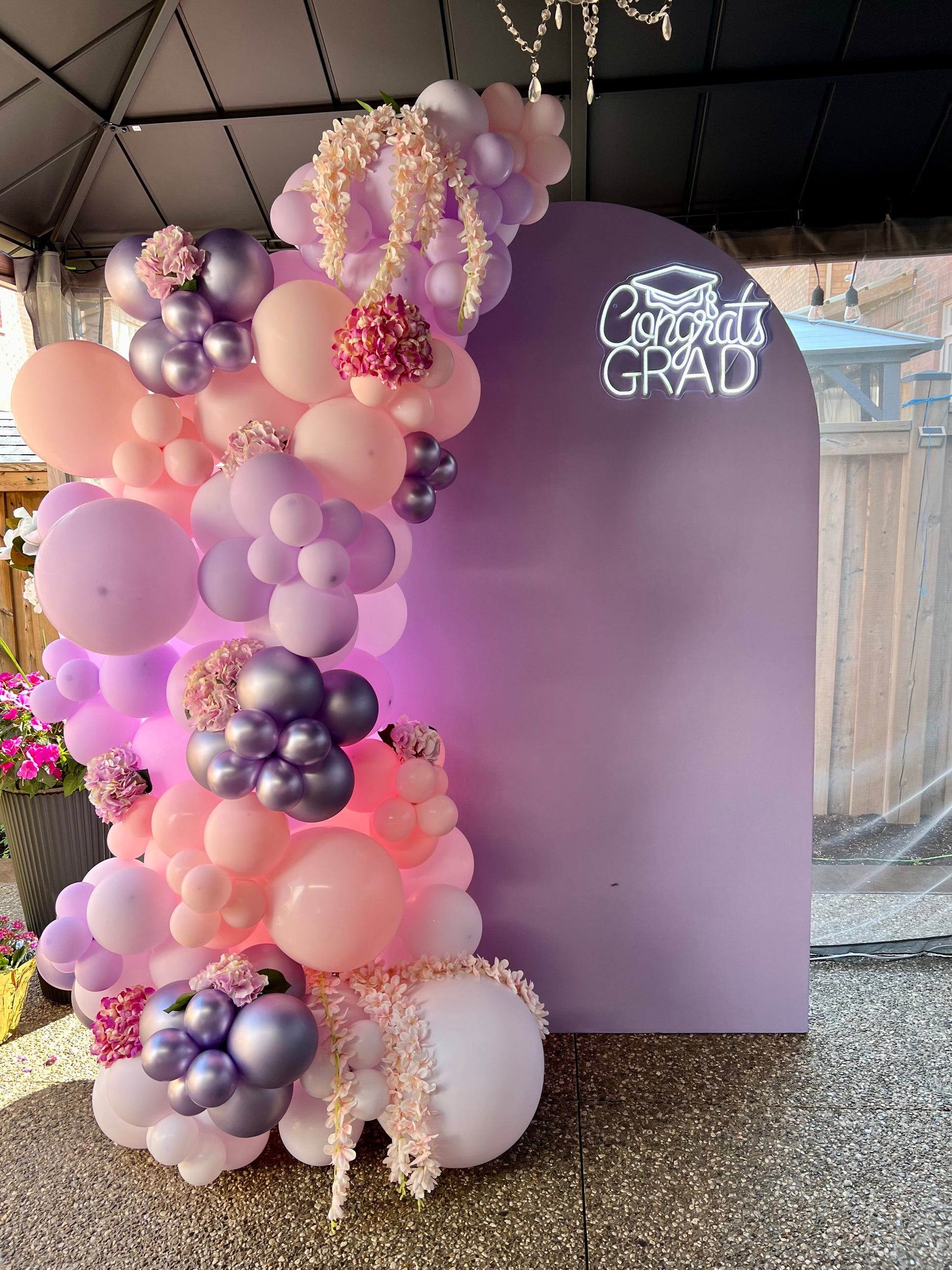Decorative balloon arch with pink, purple, and white balloons against a 'Congrats Grad' backdrop.
