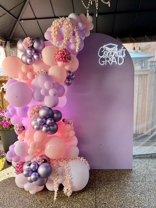 Decorative balloon arch with pink, purple, and white balloons against a 'Congrats Grad' backdrop.