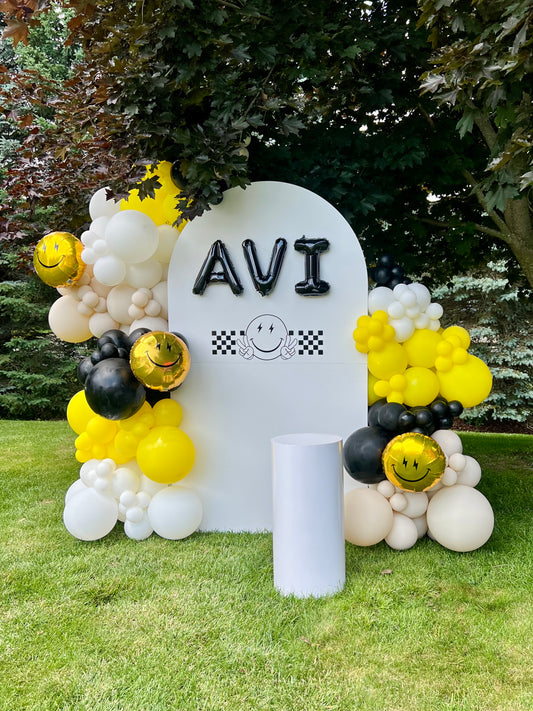 Decorative setup with balloons and a sign reading 'AVI' on a grassy area.