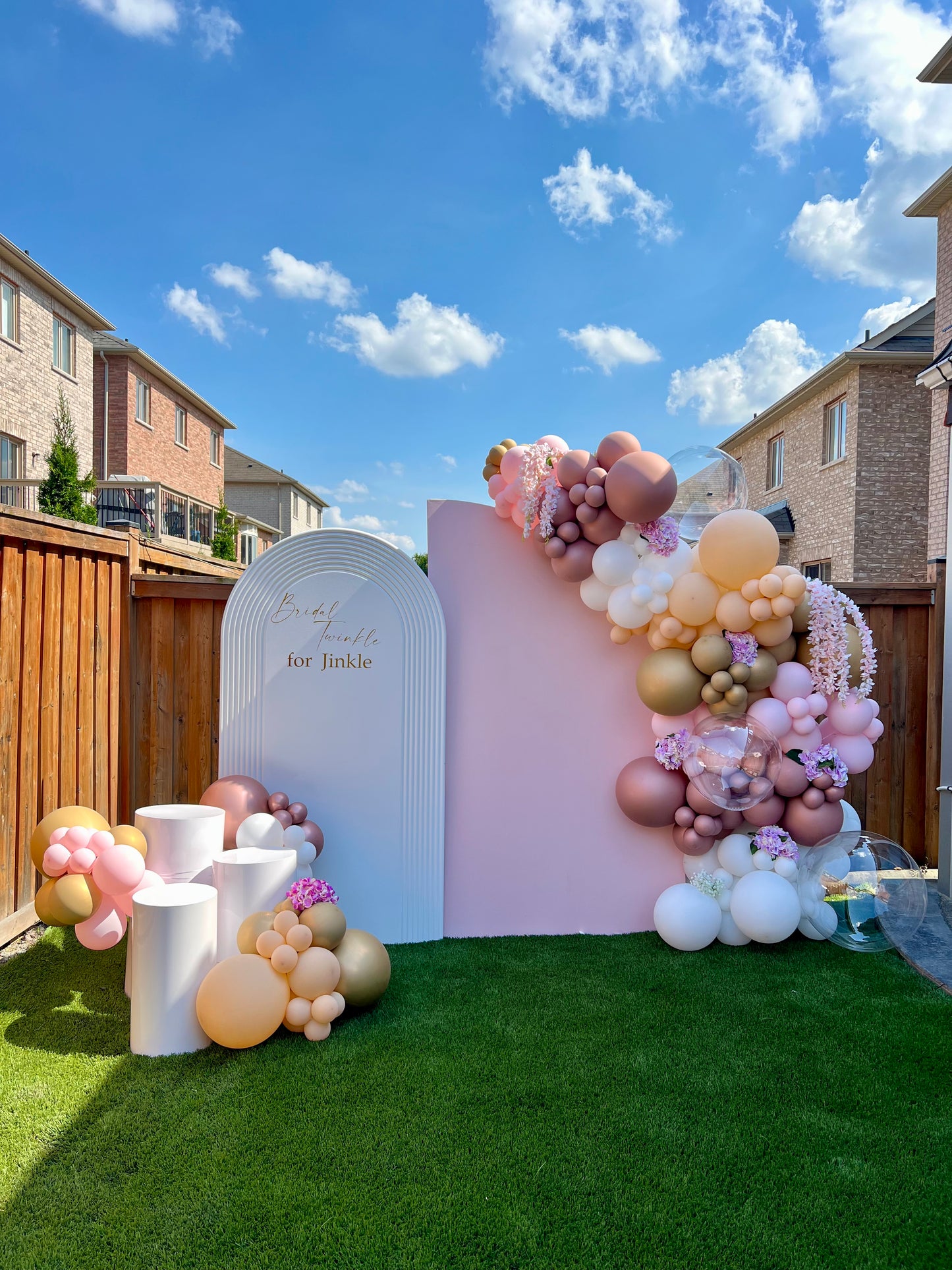 Decorative balloon arch with a pink and white backdrop in a backyard setting.