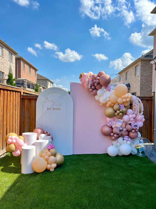Decorative balloon arch with a pink and white backdrop in a backyard setting.