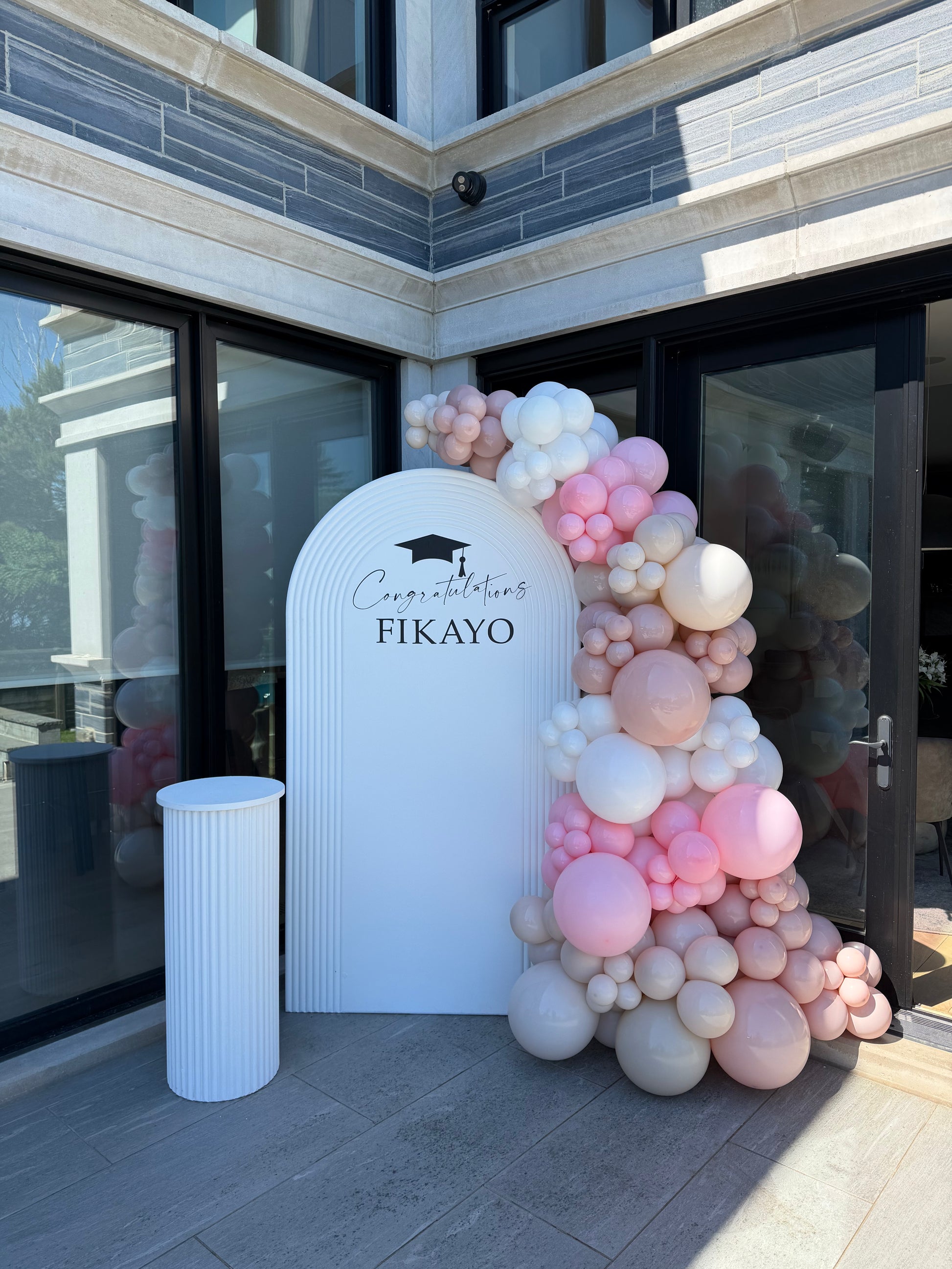 White ripple arch backdrop with blush and ivory balloon garland for a graduation celebration.