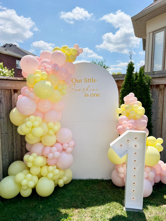 pastel first birthday balloon backdrop with pink yellow garlands and number one
