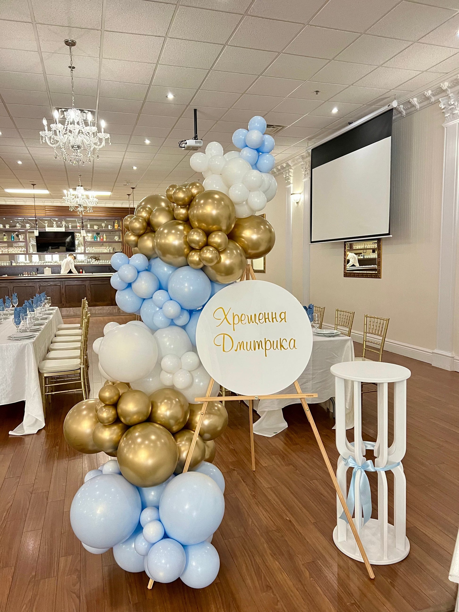Baptism easel setup with blue and white balloon garland and round sign.