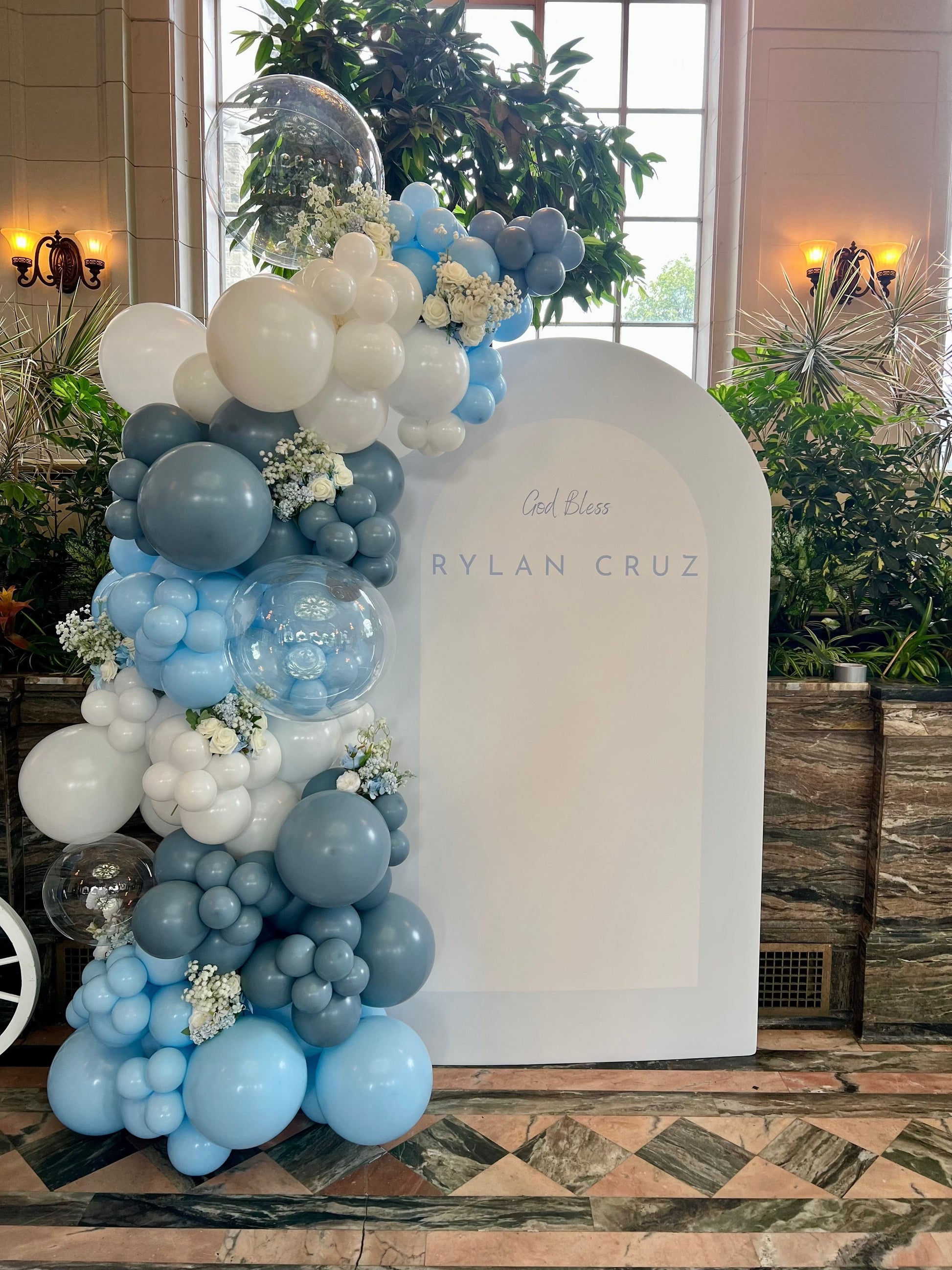 Gentle baptism backdrop setup with blue and white balloon garland and white oval backdrop