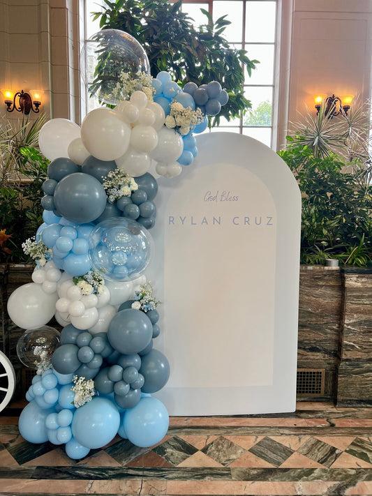 Gentle baptism backdrop setup with blue and white balloon garland and white oval backdrop