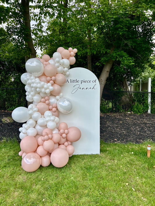 Blush baby shower setup with white oval backdrop and pearl balloon garland