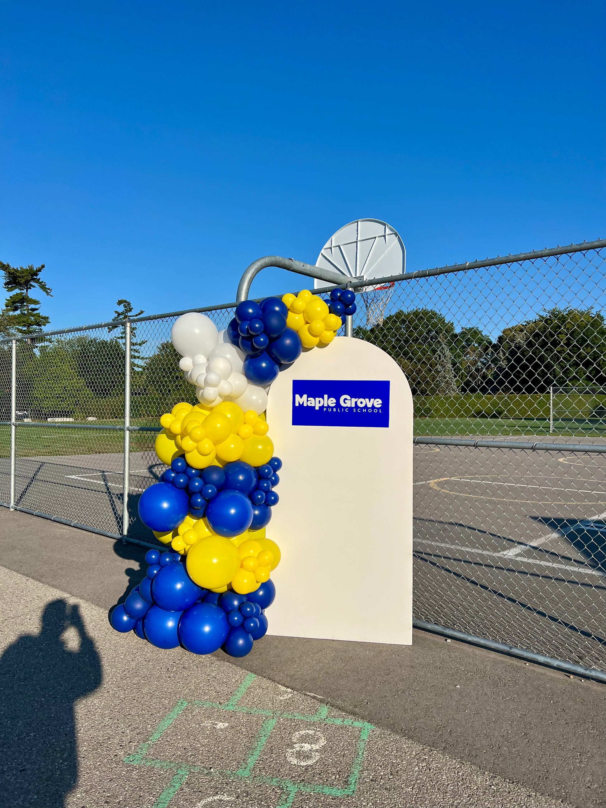 School-themed balloon setup with white arch backdrop, one-sided garland, and custom school logo sign for first-day celebration