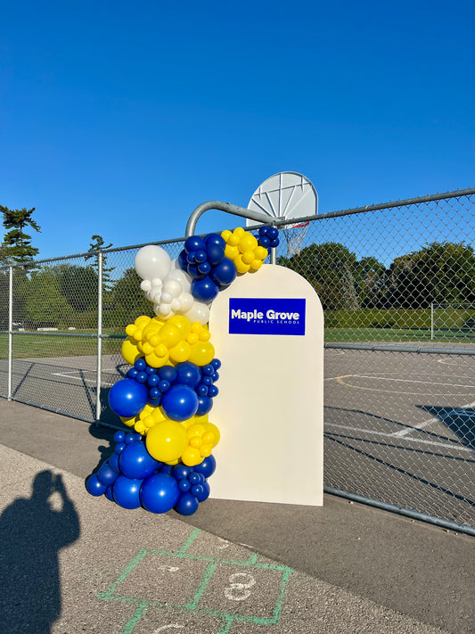 School-themed balloon setup with white arch backdrop, one-sided garland, and custom school logo sign for first-day celebration