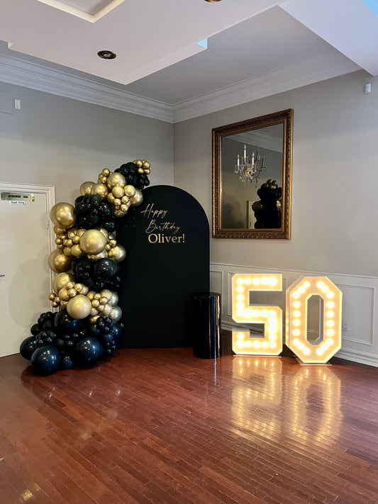 50th birthday black gold balloon backdrop with marquee numbers and cake table