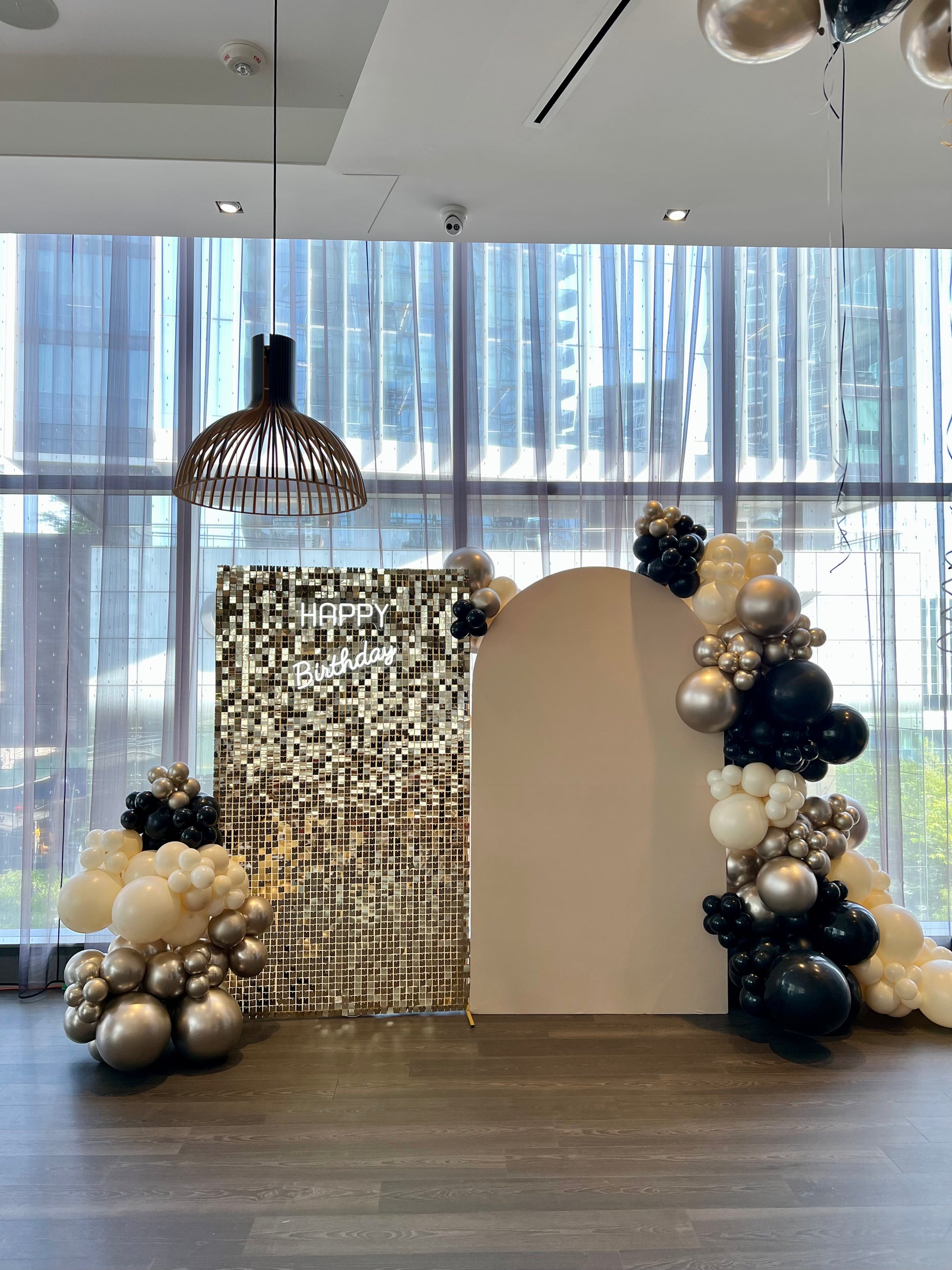 beige arch and gold shimmer wall birthday backdrop with black gold balloons