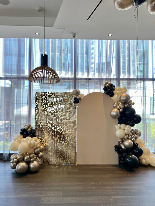 beige arch and gold shimmer wall birthday backdrop with black gold balloons