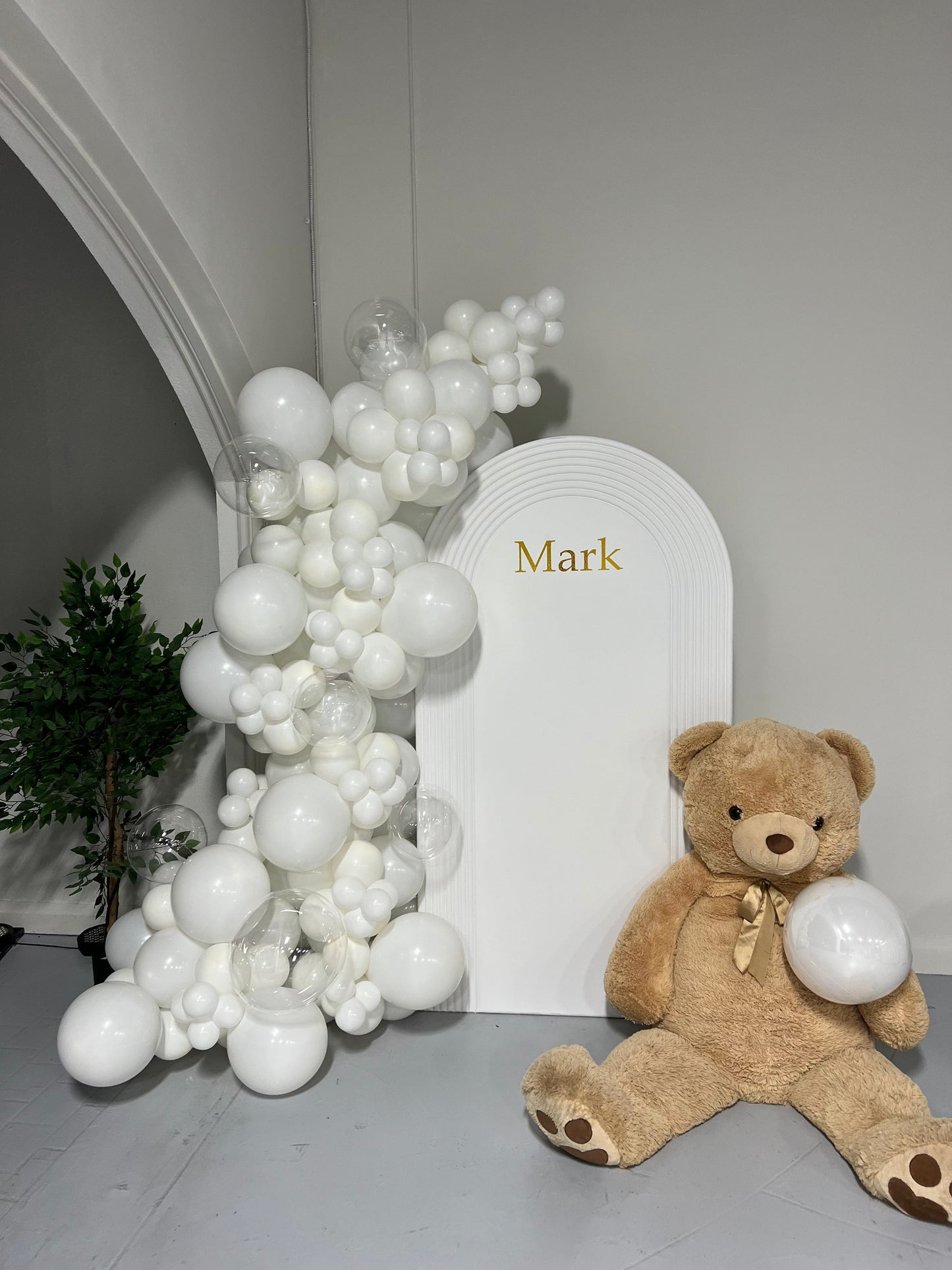 White baptism backdrop with teddy bear and all-white balloon garland.