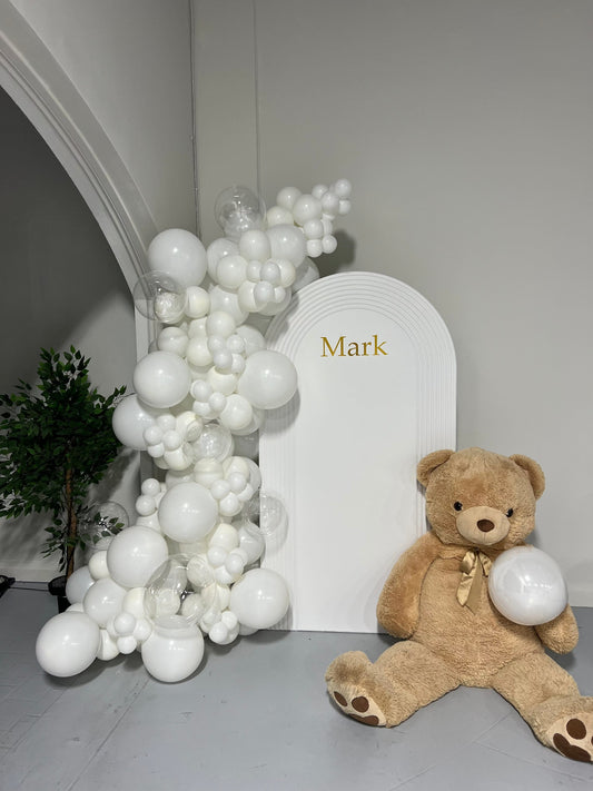 White baptism backdrop with teddy bear and all-white balloon garland.