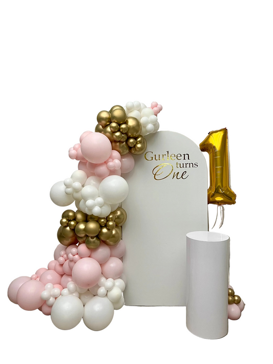 Balloon arch with pink, gold, and white balloons against a backdrop with 'Gurleen turns One' text.