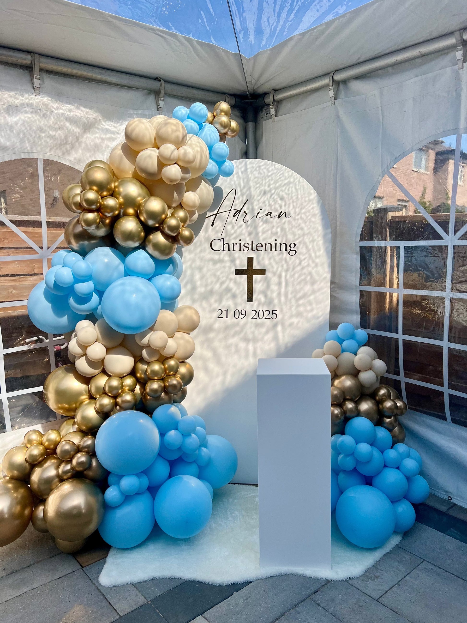 Baptism setup for boy with blue, gold, and cream balloon garlands and white oval backdrop.