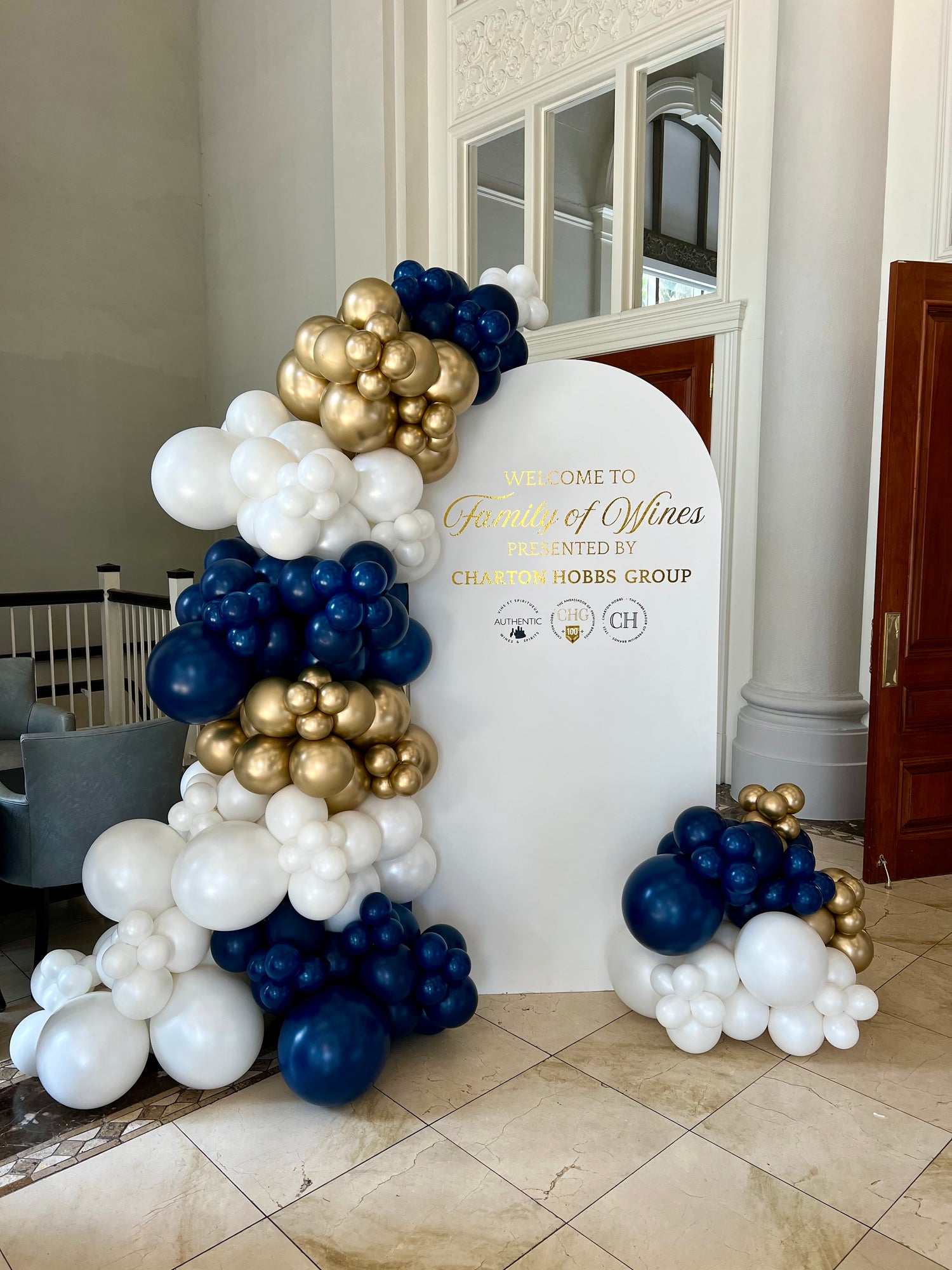 Corporate balloon installation in navy, gold, and pearl with white full arch backdrop and custom company logo for wine tasting event