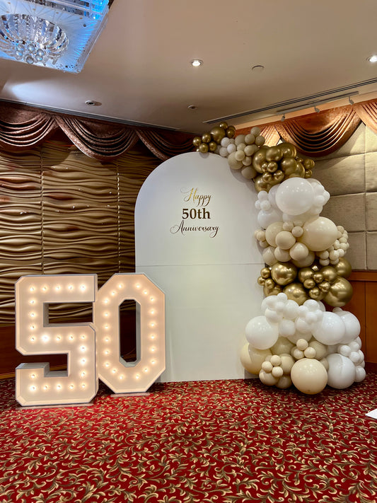 50th anniversary balloon backdrop with white arch gold garland and marquee numbers

