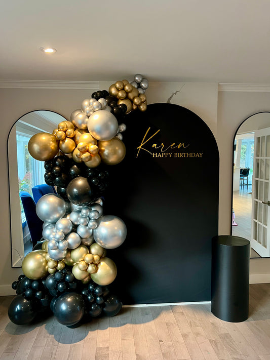 Balloon arch with gold, black, and silver balloons against a black backdrop with 'Karen Happy Birthday' text.