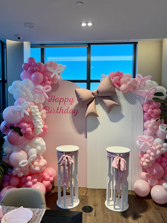 double birthday balloon backdrop with pink garlands and two cake tables
