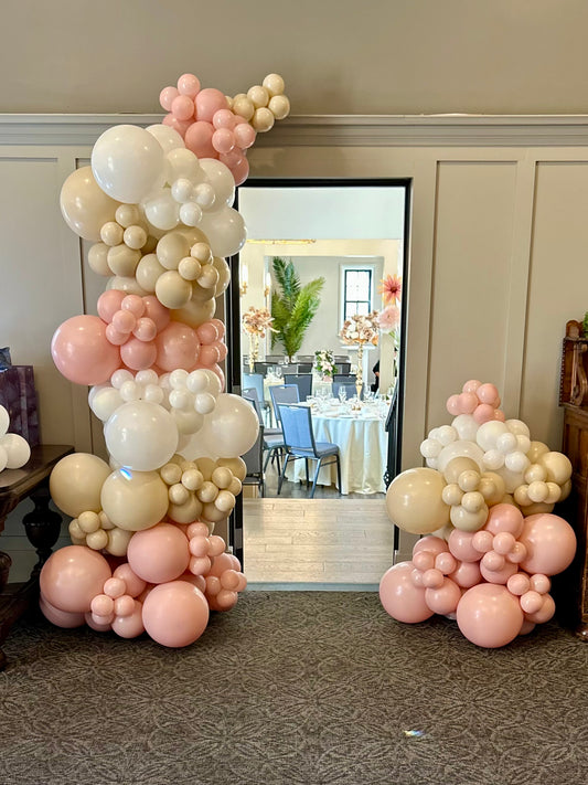 Balloon arches in pink, white, and beige colors in a room setting.