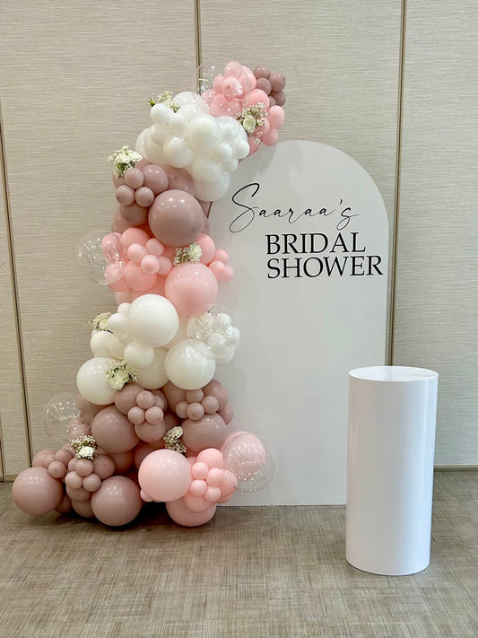 bridal shower white arch backdrop with blush balloon garland and flowers
