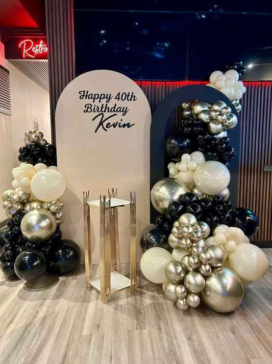 black and gold milestone birthday backdrop with beige arch, black hollow panel and luxury balloon garlands