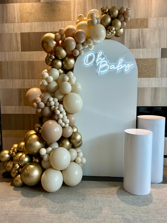 Baby Shower setup with white Full Arch backdrop, neutral balloon garland, “Oh Baby” neon sign and two cake tables