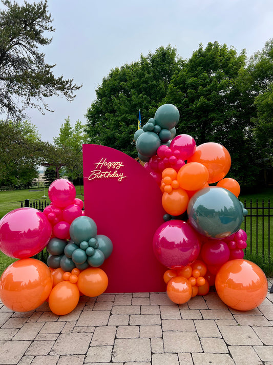 Fuchsia half-circle backdrop with LUX balloon garlands, giant clear balloons, and “Happy Birthday” neon sign