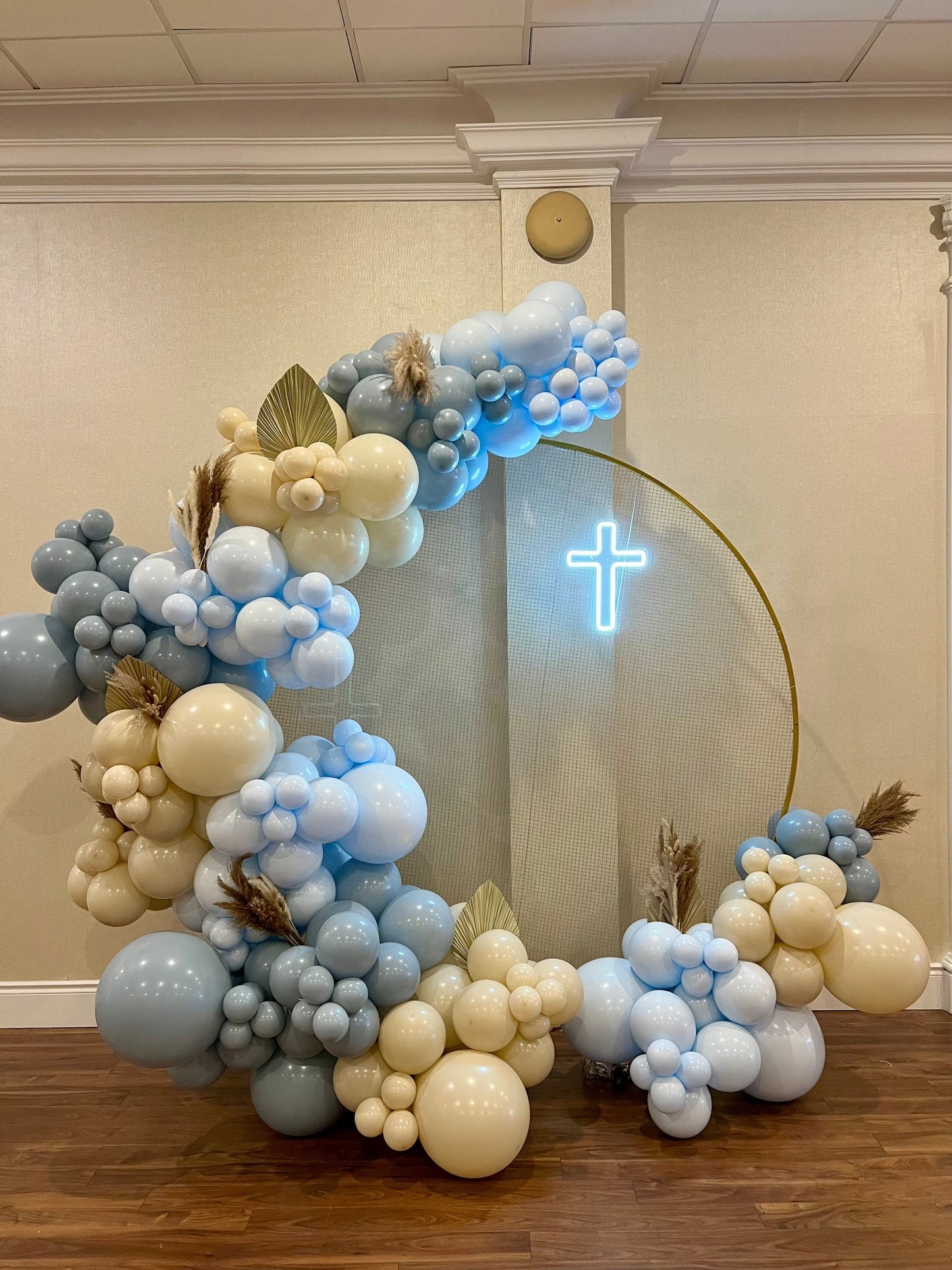 Baptism round backdrop setup with blue and beige balloons and neon cross.