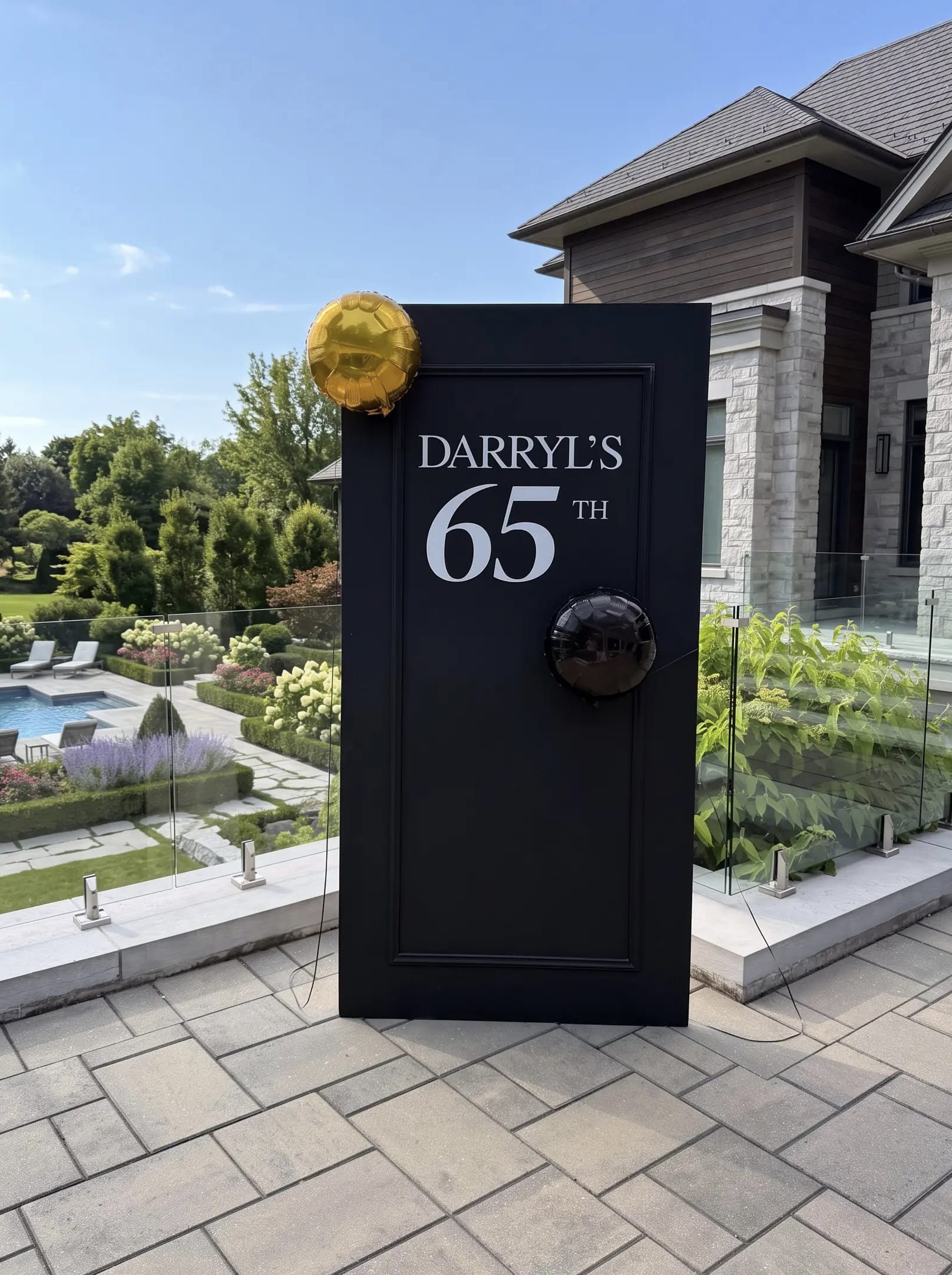 Black milestone birthday backdrop with framed panel detailing, custom white name and age lettering, and minimal gold and black balloon accents.