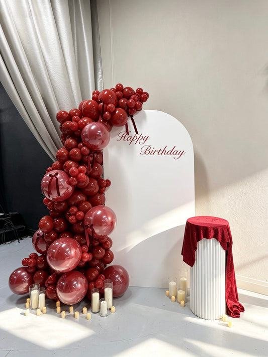 Ruby red birthday backdrop with monochrome balloon garland, transparent balloons and candle styling