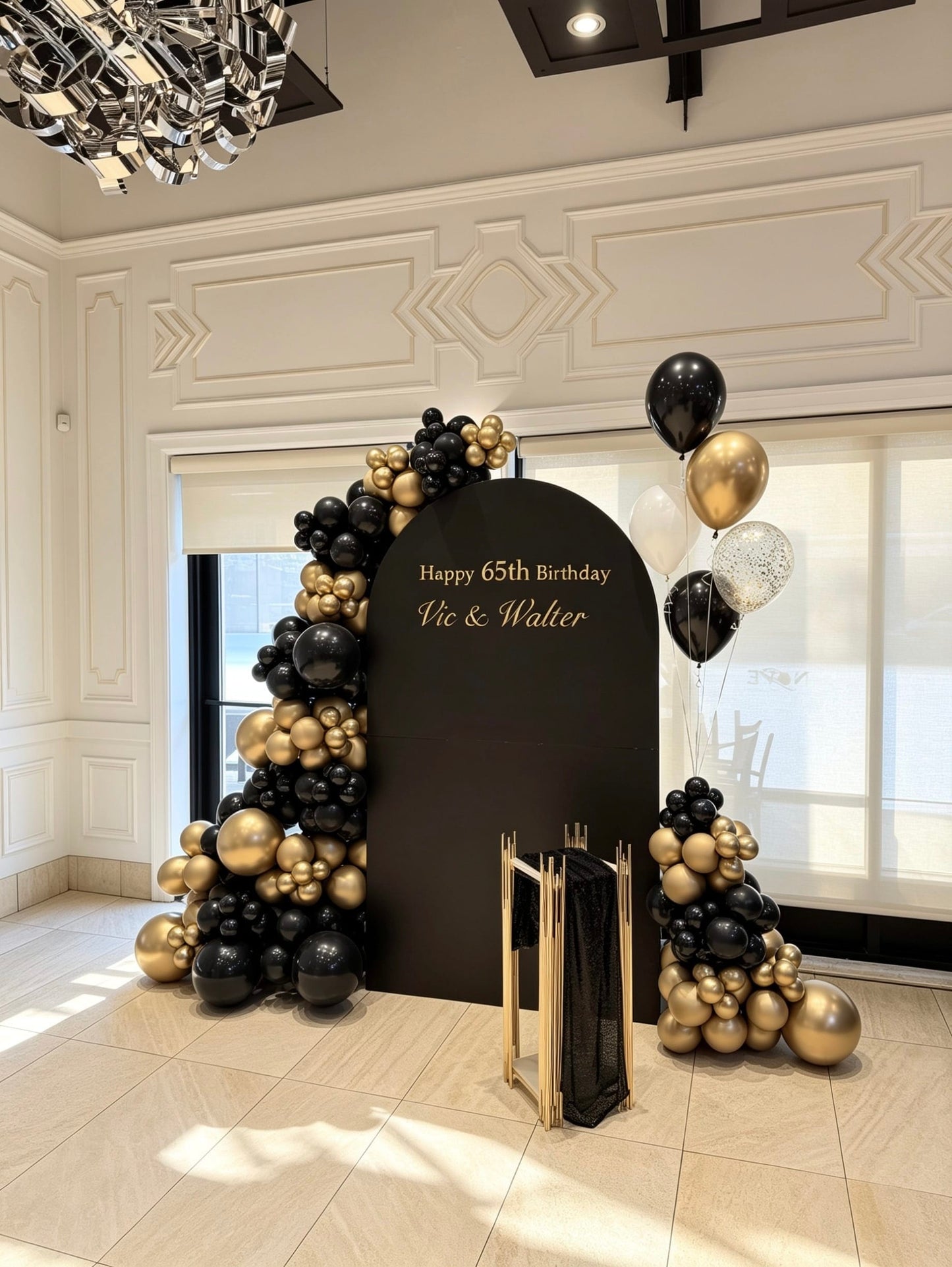 Elegant black and gold 65th birthday setup with black full arch backdrop, organic balloon garlands, helium balloons, and gold pedestal stand.