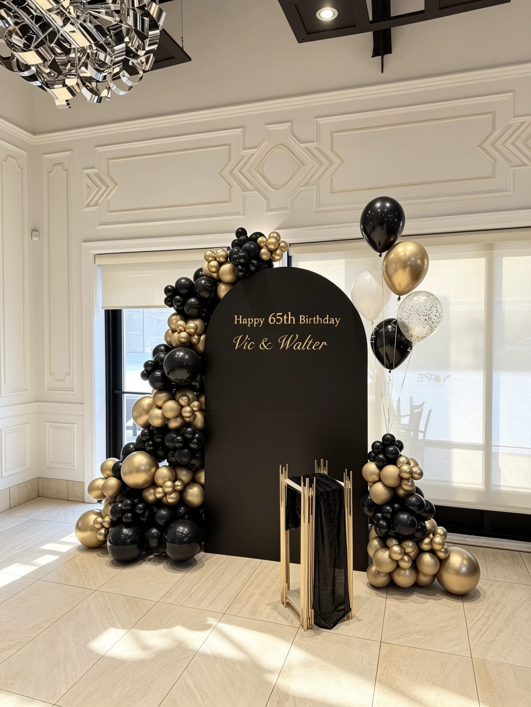 Elegant black and gold 65th birthday setup with black full arch backdrop, organic balloon garlands, helium balloons, and gold pedestal stand.